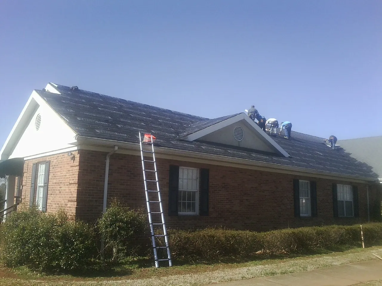 Crew tearing shingles off a brick ranch roof with a ladder set — Metal Roof Repair work by our crew in East Palestine