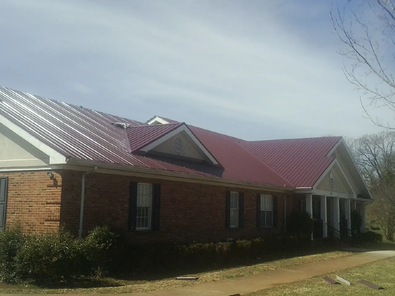 Red metal roof with gabled entries on a long brick building, from a Hail Damage Roof Repair job in East Palestine
