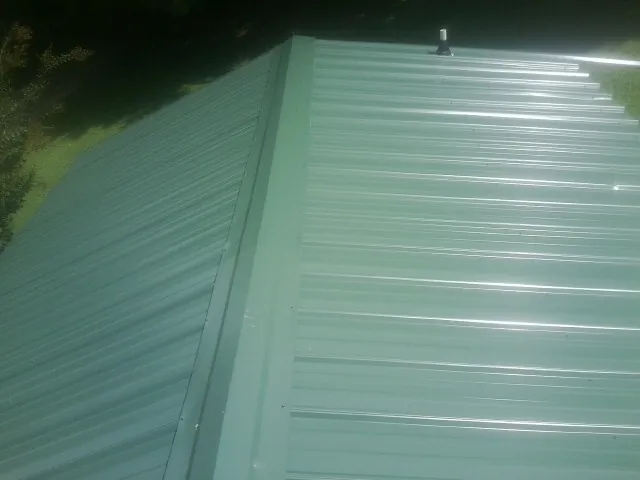 New green metal panels meeting at the ridge of a roof — Flat Roof Repair work by our crew in East Palestine