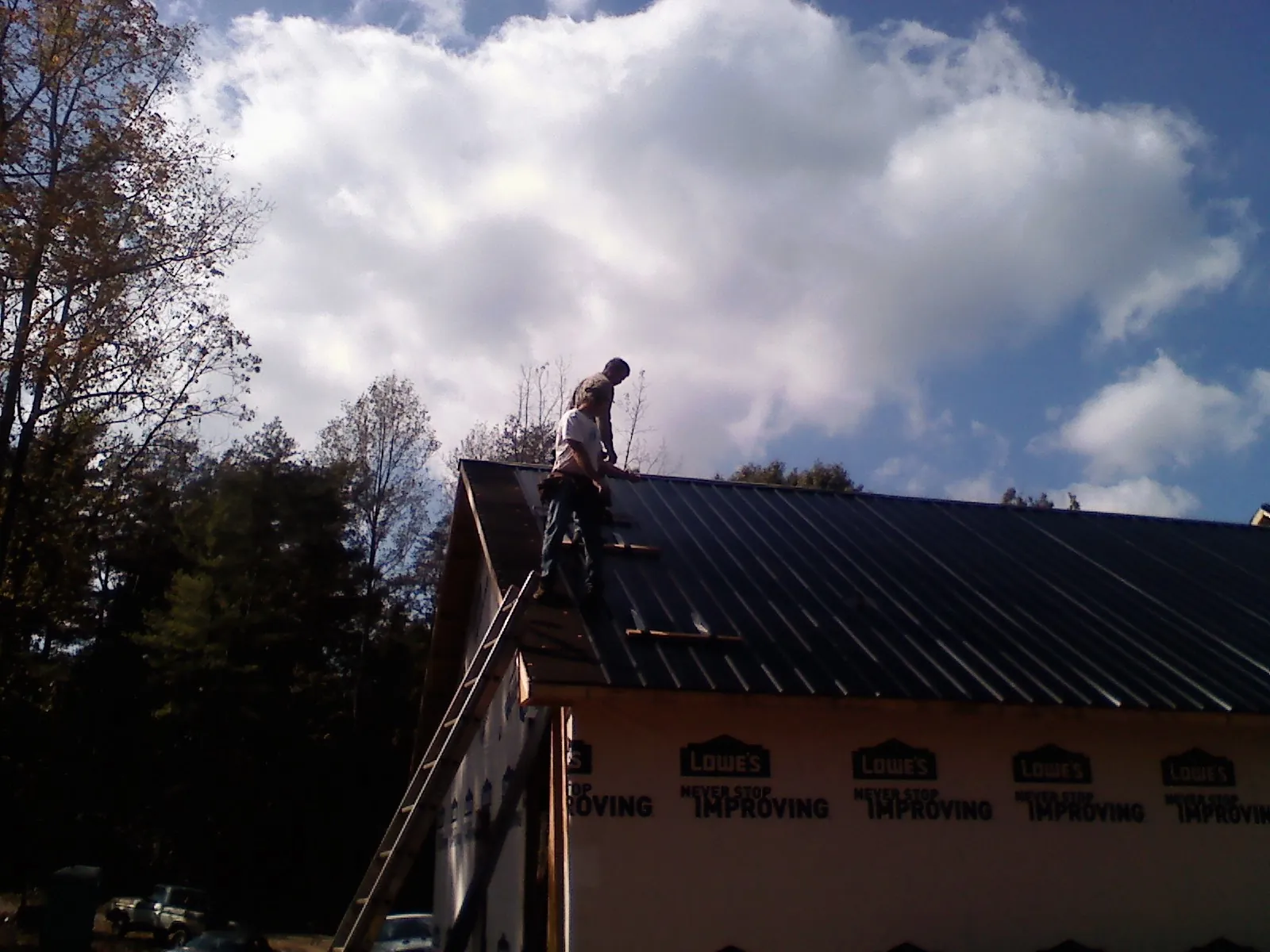 Roofer fastening dark metal panels high against a cloudy sky, from a Roof Inspection job in East Palestine