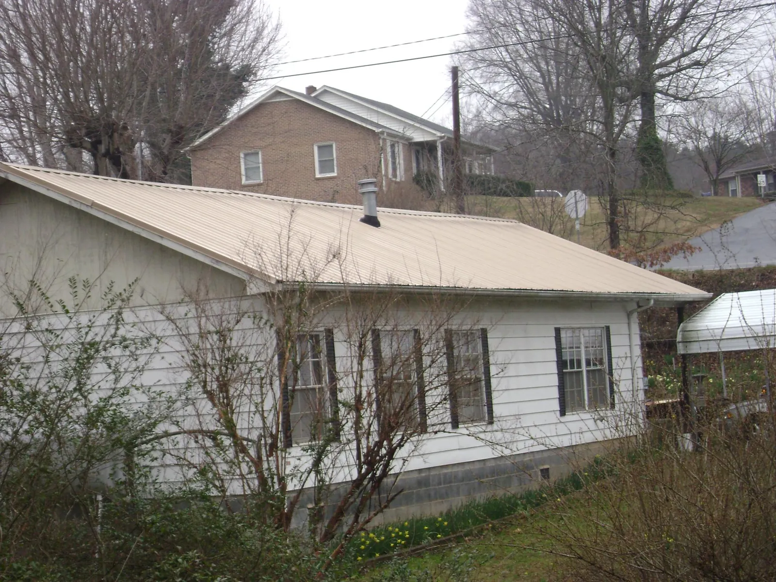 Tan metal roof on a white sided house set into a hillside — Commercial Roofing by Roofing Brothers in East Palestine