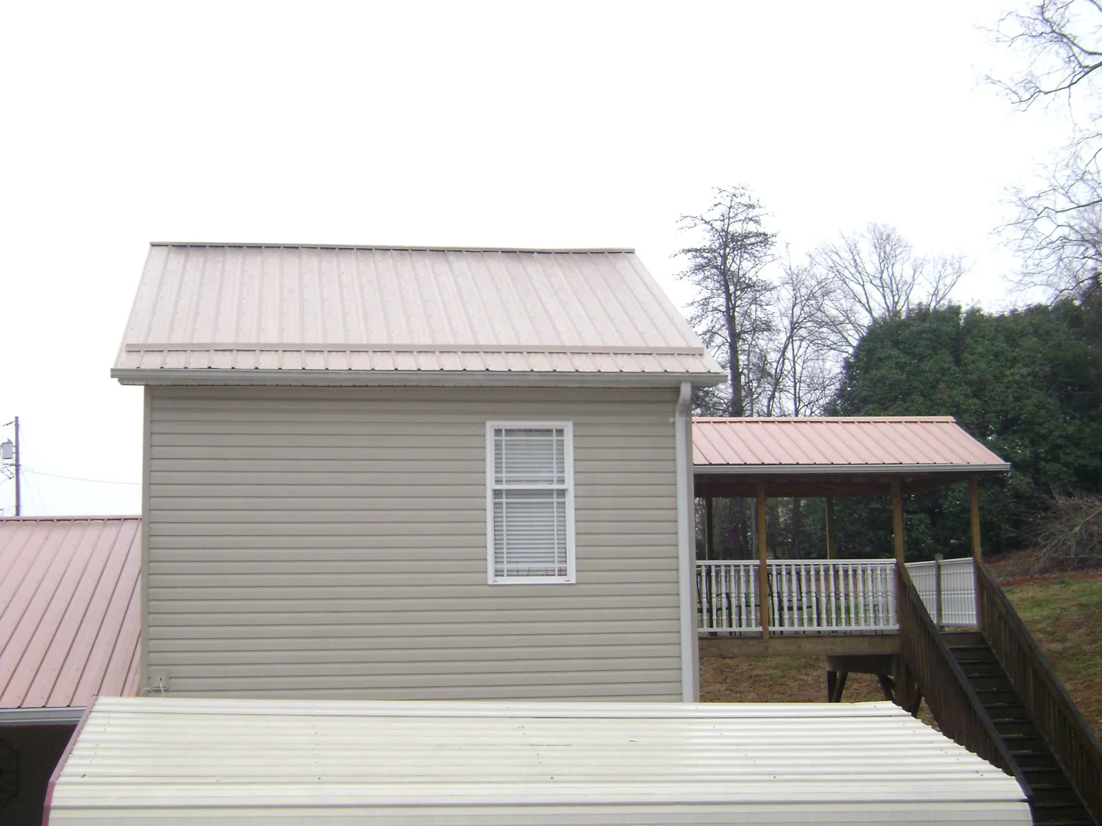 Tan metal roofs on a two story addition and attached porch, from a Roof Replacement job in East Palestine